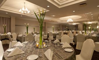 a large dining room with round tables covered in white tablecloths , and a centerpiece of tall vases containing flowers at Holiday Inn Laval - Montreal