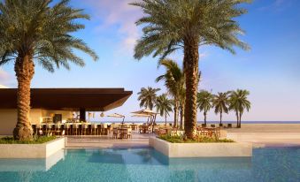 a beautiful outdoor pool area with palm trees and a beachfront restaurant , under a blue sky at Nobu Hotel Los Cabos