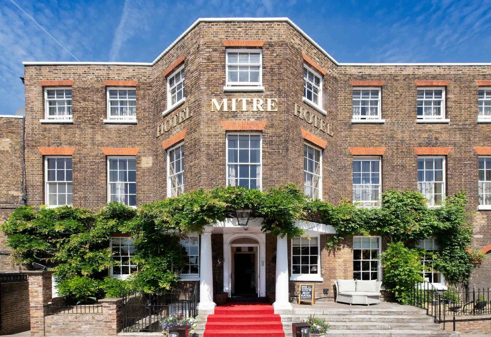 the exterior of a brick building with a red carpet leading to the entrance and trees surrounding it at Small Luxury Hotels of the World - the Mitre Hampton Court