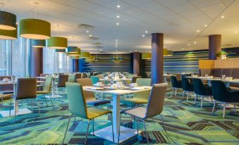 a modern restaurant with blue and green chairs , tables , and pendant lights , creating a clean and inviting atmosphere at Radisson Blu Hotel and Conference Cente, Oslo Alna