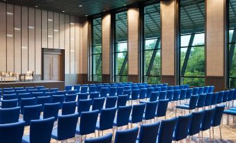 a large conference room with rows of blue chairs arranged in a semicircle , facing a large window at Le Meridien Chiang Rai Resort, Thailand