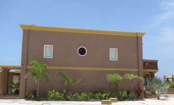 a brown building with a circular window and yellow trim , surrounded by palm trees and plants at Kings Point