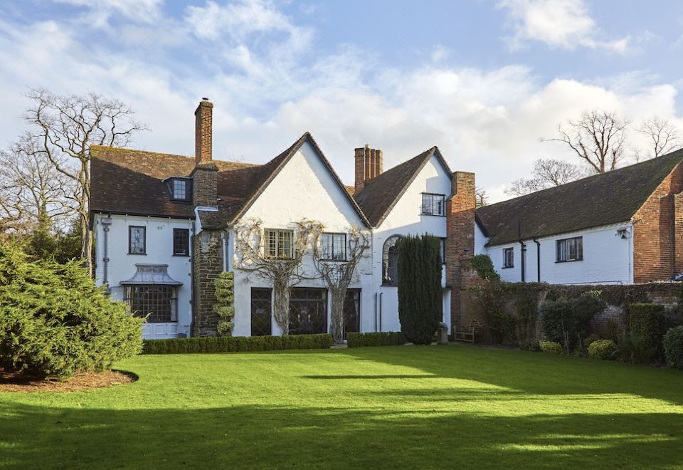 a large white house surrounded by a lush green lawn , with trees and bushes in the background at B&B Harlington Manor