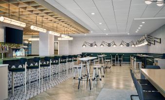 a modern restaurant with white walls , gray floors , and black and white tiled accents , featuring a bar area with stools and tables at Delta Hotels Muskegon Convention Center