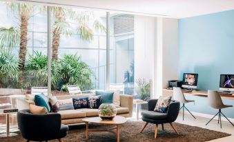 a modern living room with a couch , chairs , and a tv . also a dining table in the room at Saint Kilda Beach Hotel, an EVT hotel - Formerly Rydges St Kilda