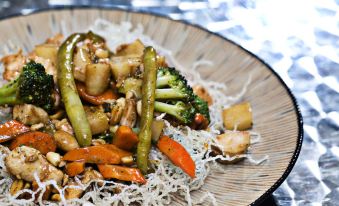 a plate of stir - fried vegetables and meat , including broccoli , carrots , and chicken , sits on a dining table at Flamingo Hotel