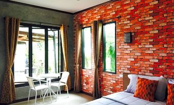 a modern bedroom with a large window , brick wall , and white bed , along with a table and chairs at Khun Naparn Resort