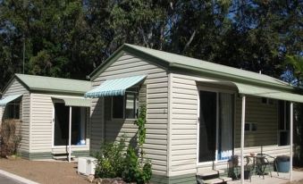 a row of two small , green - roofed cabins with a blue awning and potted plants in front at BIG4 Hervey Bay Holiday Park