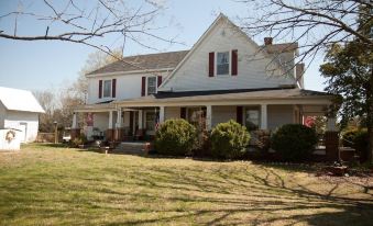 a large white house with a red roof and a porch is surrounded by green grass at Lamplight Inn