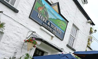 "the exterior of a white building with a sign that says "" hare and hounds country inn "" and flowers on the side" at Hare and Hounds