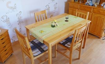 a wooden dining table with a green striped tablecloth and four chairs , set against a white wall with drawings at Gila