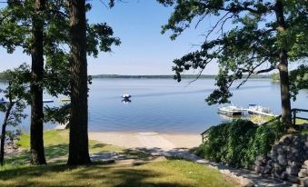 a serene lake scene with a boat floating on the water , surrounded by trees and a sandy beach at Kohl's Resort