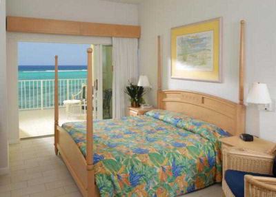 a bedroom with a large bed , a dresser , and a door leading to a balcony overlooking the ocean at Wyndham Reef Resort Grand Cayman