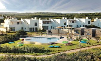 a large white building with a swimming pool in front of it , surrounded by grass and trees at Martinhal Sagres Beach Family Resort Hotel