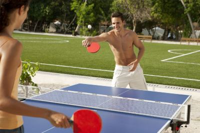 a man is playing table tennis on a blue table with a net in the middle at Vilamendhoo Island Resort & Spa