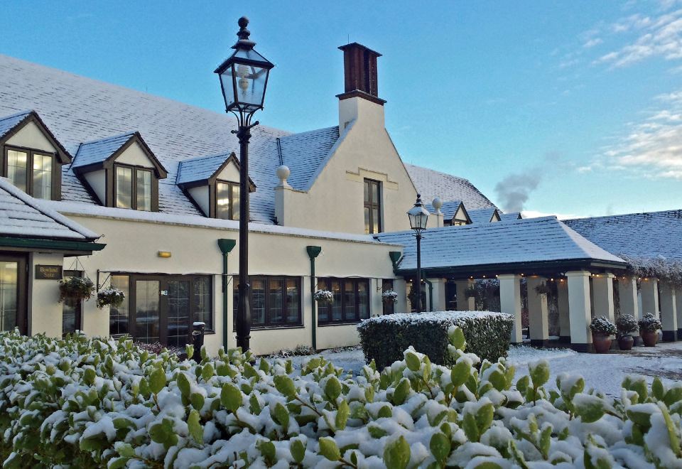 a snow - covered building with a green light post in front , surrounded by snow - covered bushes and trees at Lancaster House Hotel