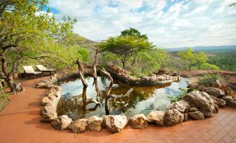 a serene outdoor setting with a pond surrounded by rocks , trees , and a gazebo , creating a picturesque atmosphere at Leopard Mountain Safari Lodge
