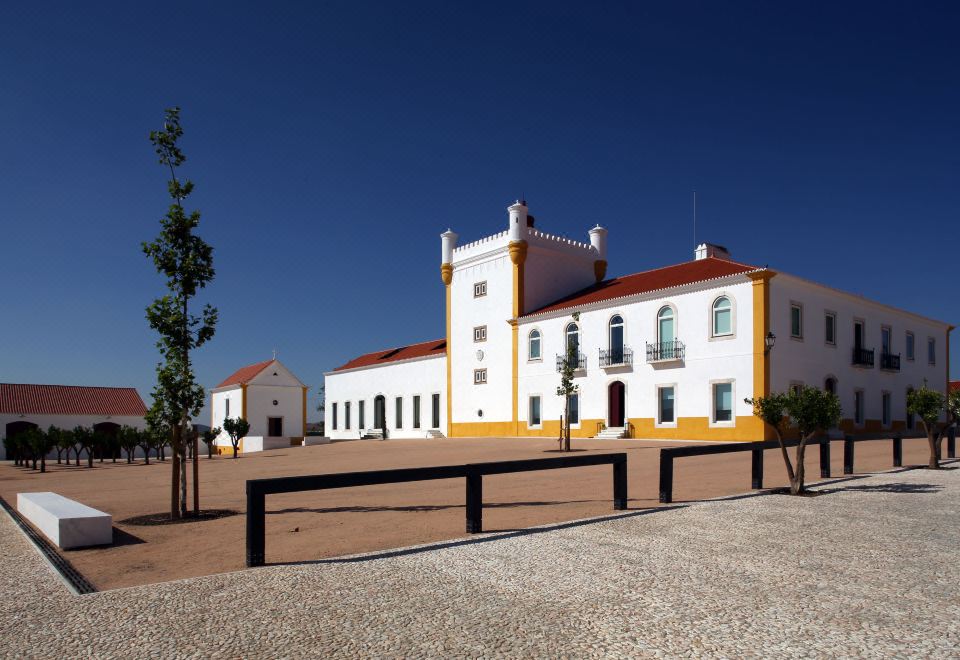 a large white building with a red roof and two towers is surrounded by a gravel lot at Torre de Palma Wine Hotel, Montforte, a Member of Design Hotels