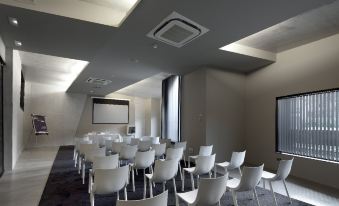 a conference room with rows of white chairs arranged in a semicircle , and a projector screen mounted on the wall at Hotel Viura