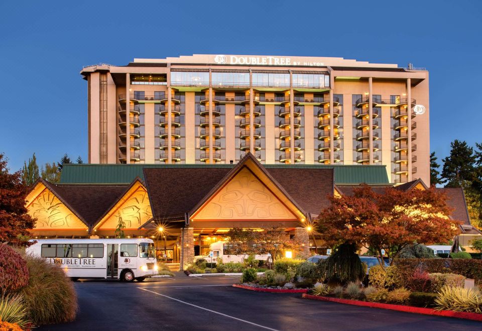 a large hotel building with a parking lot in front of it , illuminated at dusk at DoubleTree by Hilton Seattle Airport