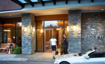 a man and a woman are standing outside a hotel entrance with a car parked in front at Oswego Hotel