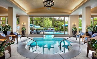 a large indoor pool with a circular design , surrounded by chairs and umbrellas , and a chandelier hanging from the ceiling at Fairmont Chateau Whistler