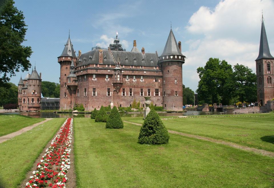 a large red brick castle surrounded by green grass and flowers , with trees in the background at Fletcher Hotel Restaurant Loosdrecht-Amsterdam