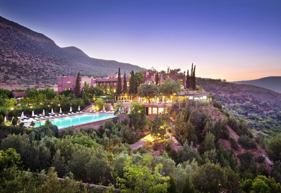 a resort with a large pool surrounded by lush greenery and mountains in the background at Kasbah Tamadot