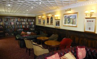 a cozy living room with couches , chairs , and a bookshelf filled with books , creating a warm and inviting atmosphere at The Atherstone Red Lion Hotel