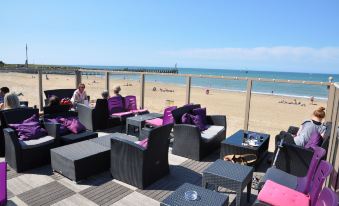 a group of people sitting on black chairs on a patio overlooking the beach , enjoying the view at La Cremaillere