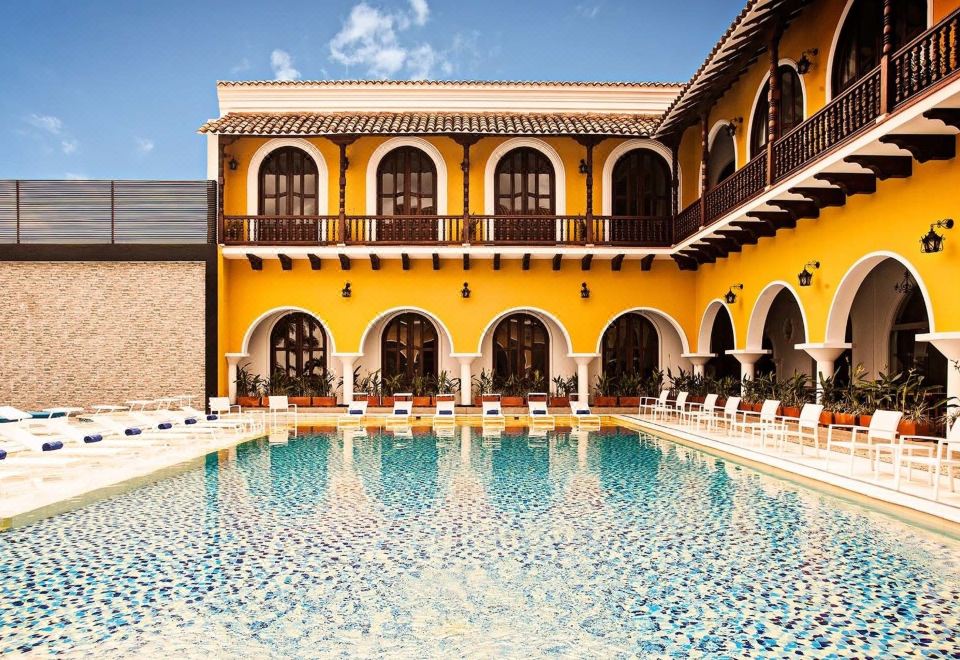 a large swimming pool surrounded by a yellow building , with several lounge chairs placed around it at Hotel Union