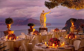 a table set for a formal dinner with white tablecloths , candles , and a statue overlooking the ocean at Hotel Caesar Augustus
