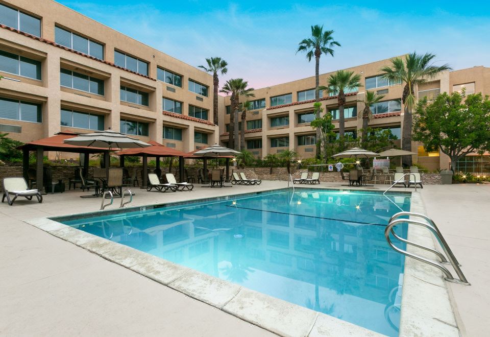 an outdoor swimming pool surrounded by a building , with several lounge chairs and umbrellas placed around the pool area at Grand Vista Hotel