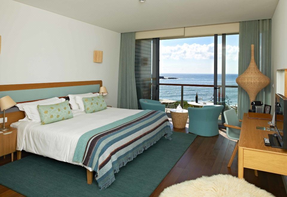 a large bedroom with a bed , chair , and sliding glass door leading to a balcony overlooking the ocean at Martinhal Sagres Beach Family Resort Hotel