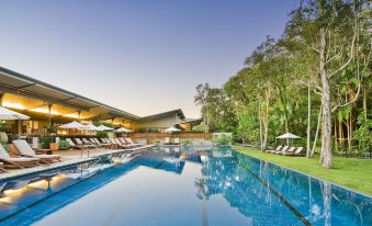 a large swimming pool with a hotel in the background and lounge chairs around it at Crystalbrook Byron