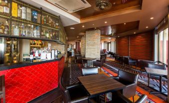 a modern bar with wooden tables and black chairs , a red - themed wall , and a large window at Rydges Southbank Townsville, an EVT hotel