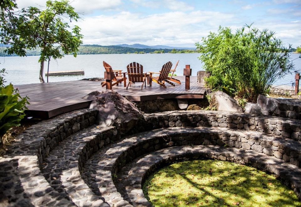 a serene outdoor setting with a view of a lake and mountains , featuring two adirondack chairs , a pond , and a circular seating area at Jicaro Island Lodge Member of the Cayuga Collection