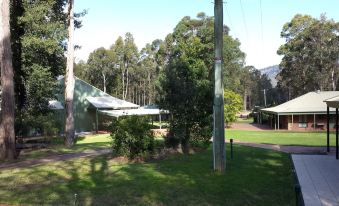 a sunny day in a park with trees , grass , and a house surrounded by bushes at Hunter Valley Retreat
