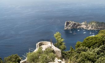 a scenic view of the mediterranean sea , with boats sailing in the distance and a stone building perched on a cliff at Bordoy Continental Valldemossa