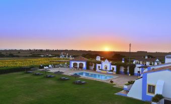a beautiful sunset over a grassy field , with a pool and several lounge chairs surrounding it at Herdade Do Touril