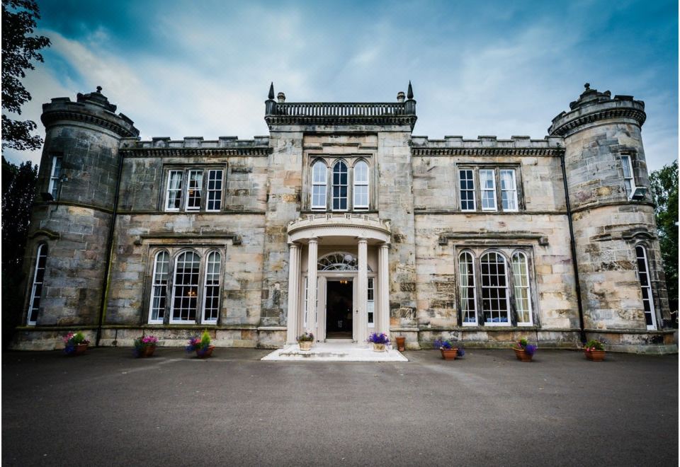 a grand stone building with multiple windows and doors , set in a courtyard with clear skies at Kincaid House Hotel