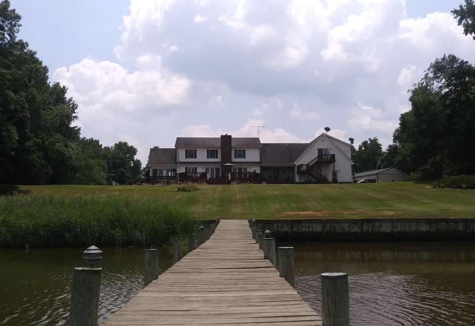 a large house is situated on a grassy field , with a wooden dock extending into the water at Marvels on the Creek