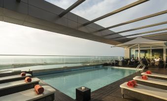 a large swimming pool is surrounded by lounge chairs and a pergola , with the ocean visible in the background at Hotel Baia