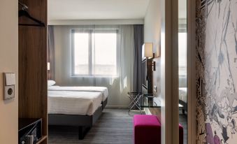 a modern hotel room with two beds , a window , and a red bench near the door at Moxy Edinburgh Airport