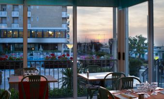 a dining area with tables and chairs , as well as a view of the sunset through a window at Hotel Miramare