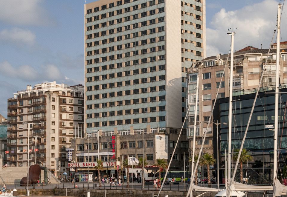 a large building with many windows is surrounded by tall buildings and sailboats in the water at Hotel Bahía de Vigo