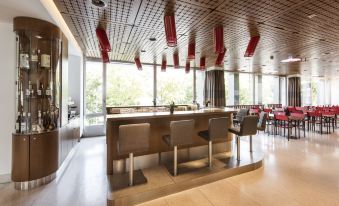 a modern restaurant with a wooden bar and chairs , surrounded by windows that offer a view of the outdoors at Hotel Ambassador