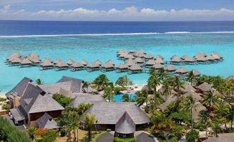 a large body of water with many palm trees and thatched huts lining the shore at Hilton Moorea Lagoon Resort and Spa