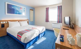 a modern hotel room with blue walls , white bedding , and a bed , along with a desk and tv at Travelodge Wincanton