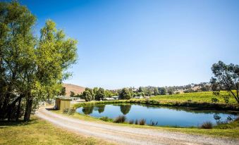 a rural landscape with a dirt road , a pond , and a house in the background at De'Vine Escape